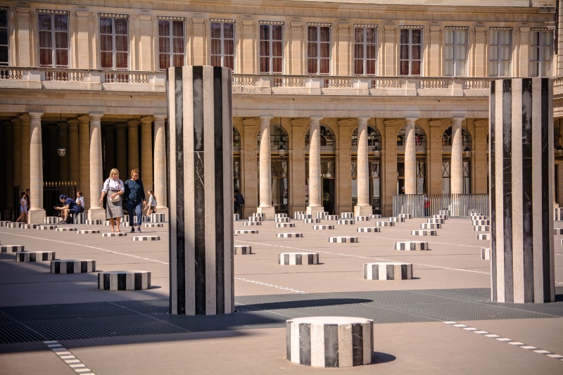 Two people walking in contemporary black and white striped octagonal columns sculptures in the courtyard of Domaine National du Palais-Royal a former royal palace in Paris, France