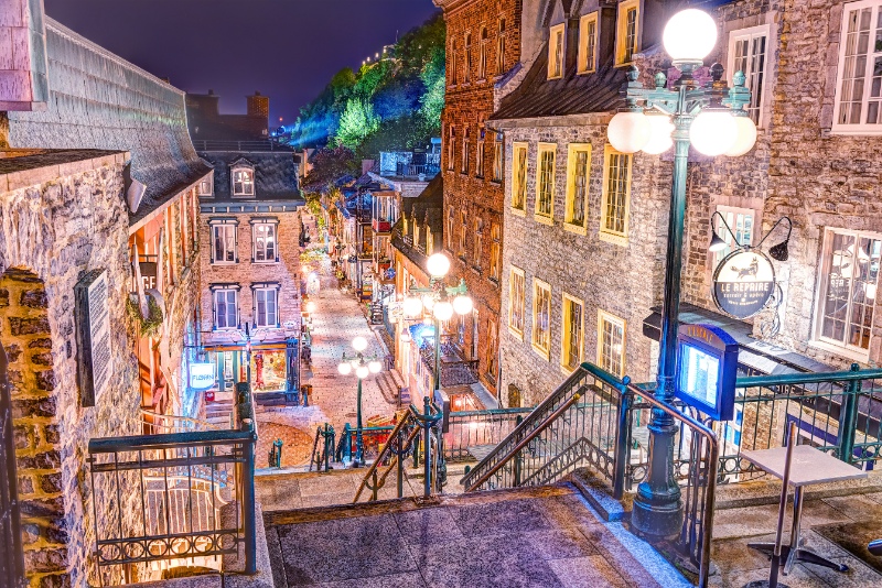 Escalier Casse-Cour on lower old town street Rue du Petit Champlain with restaurants during rainy night or twilight evening with colorful lights