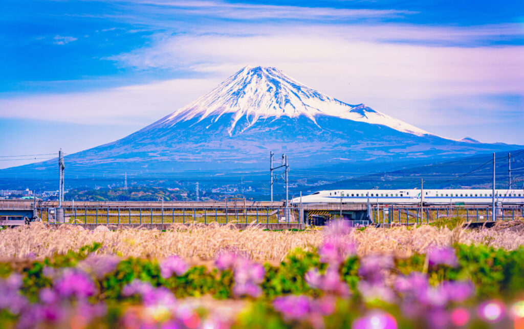 Shinkansen bullet train speeding past snow-capped Mount Fuji on clear day