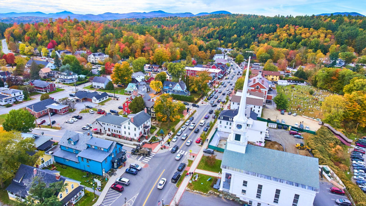 Stunning aerial over small Vermont town of Stowe surrounded by fall foliage and focus on white church