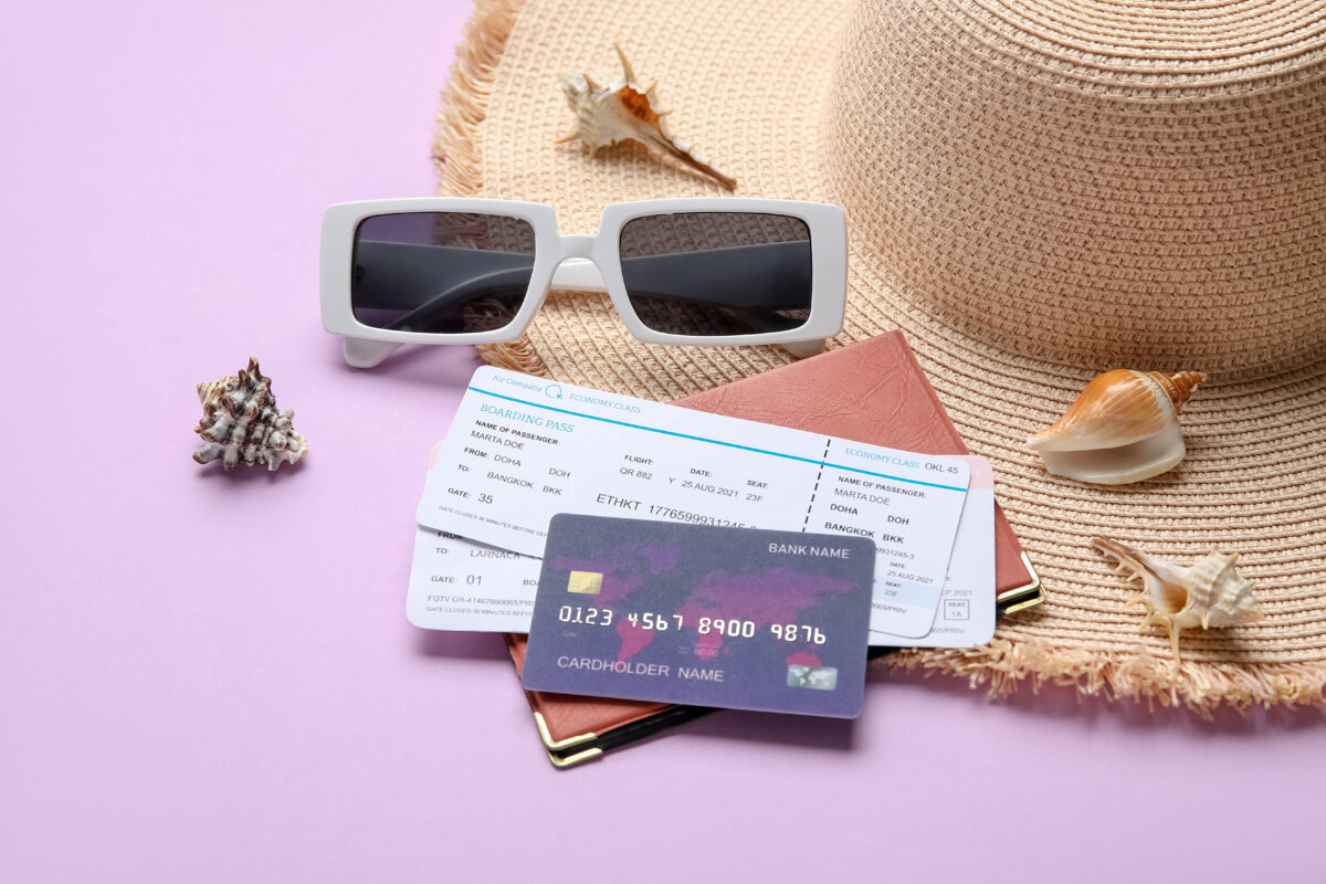 Travel credit card, passport holder, and two plan tickets with travel sunglasses and hat on the side