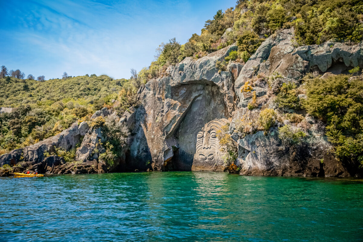 Ancient Maori rock carvings on cliffs overlooking crystal blue Lake Taupo New Zealand largest lake