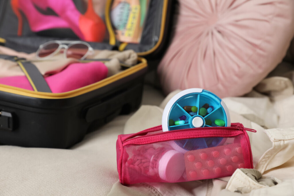 Medicine pouch filled with medications and a vitamin pill box next to an open travel suitcase