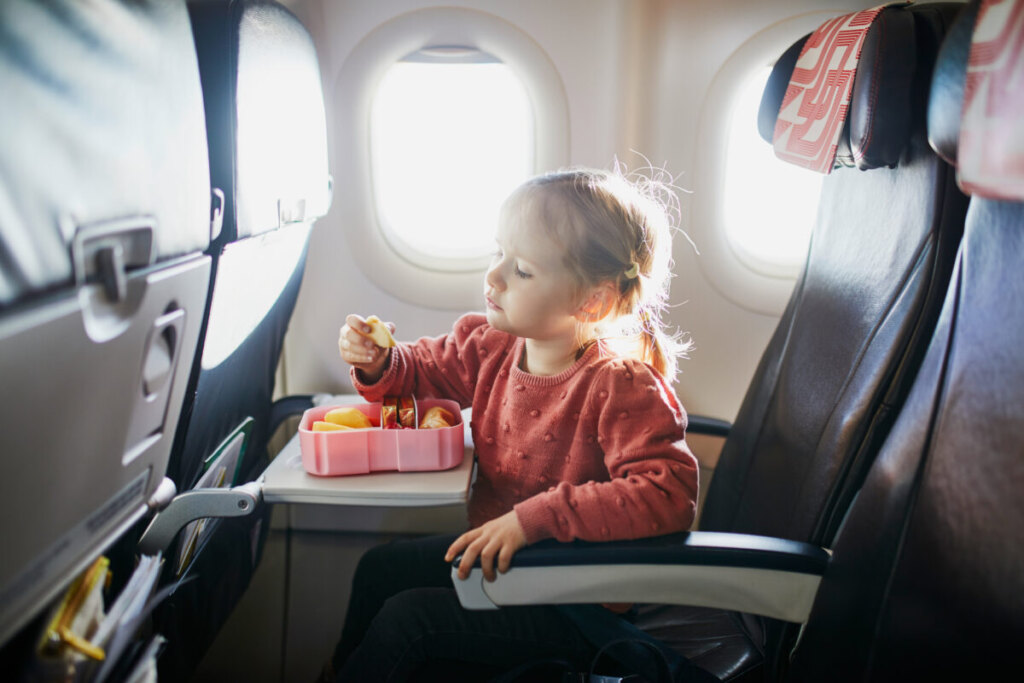 Young girl eating a packed snacks from lunch box inside a plane