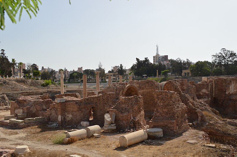 The Ancient Roman Theater of Alexandria, weathered stone ruins with rows of seating and arched entrances against a backdrop of clear skies.