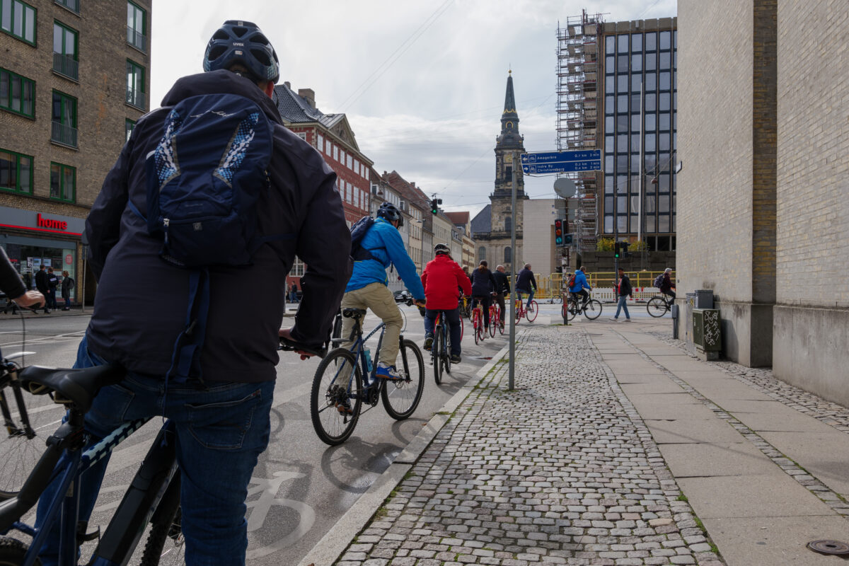 Queue of People ride bicycle, stop and wait at the intersection for traffic light on bicycle lane in Copenhagen, Denmark.