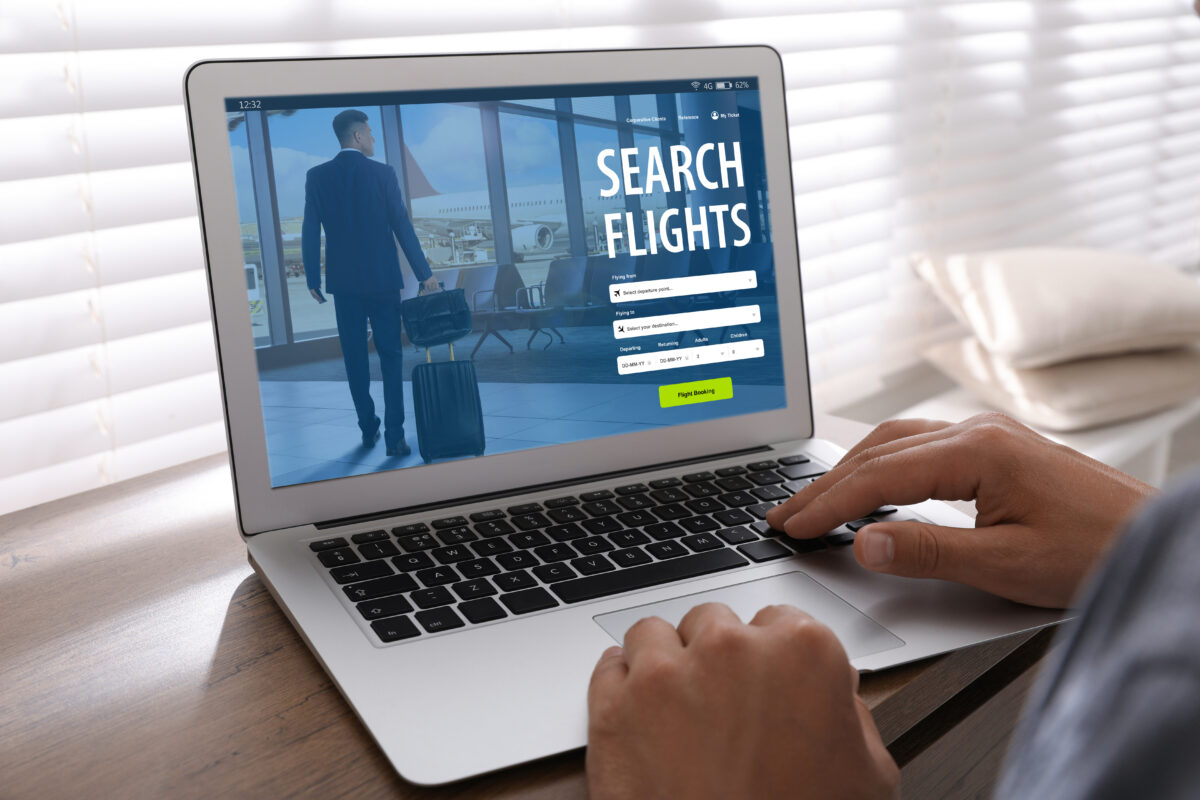 Man using laptop to book flight at wooden table, closeup