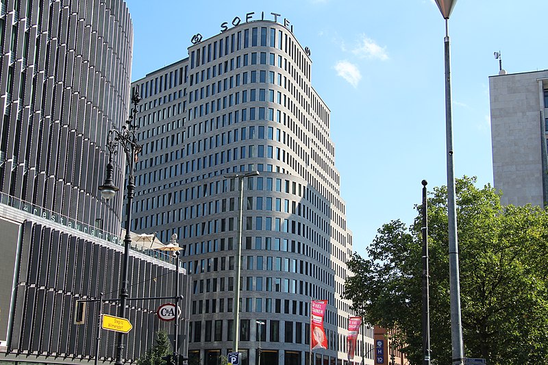A bustling scene along Kurfürstendamm (Ku'damm), the famous shopping avenue in Berlin, Germany, with pedestrians, shops, and vibrant city life.