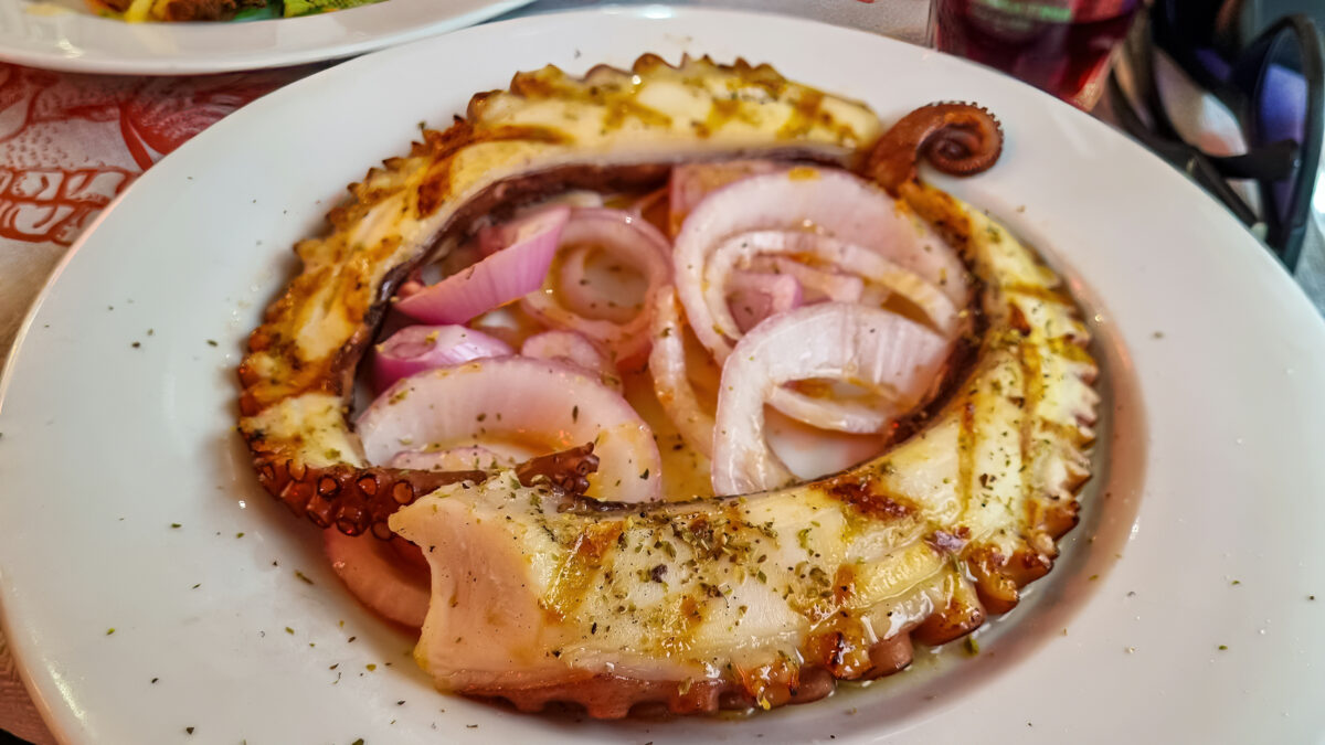 Traditional Greek grilled octopus served with onions and olive oil at a taverna in Thessaloniki, showcasing the city's renowned culinary scene
